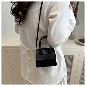 Model wearing a black micro handbag with a large arched handle in a minimalist white setting