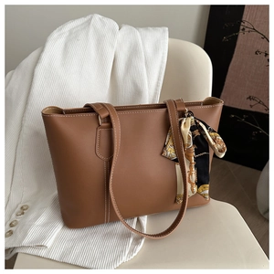 Detail view of brown leather tote bag with white contrast stitching and a silk scarf