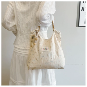 Detail of cute beige canvas shoulder bag with animal prints and plush ball pendant
