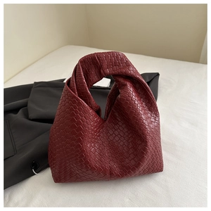 Macro shot of burgundy woven leather texture and knotted handle detail on hobo bag