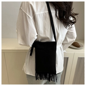 Détail d'un sac bandoulière en daim noir avec de longues franges et un style minimaliste