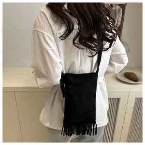 Detail of black suede fringe crossbody bag with tassel trim on model background