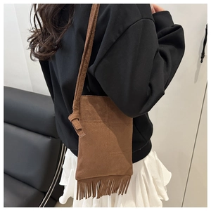 Detail of brown suede crossbody bag featuring retro fringe tassels and long slim strap