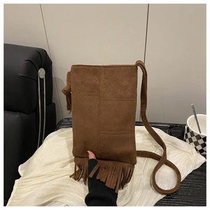 Détail d'un sac à bandoulière en daim marron avec des franges sur tissu blanc