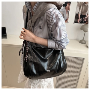 Detail of black glossy hobo bag with distinctive bell charm and woven rope knot accessory
