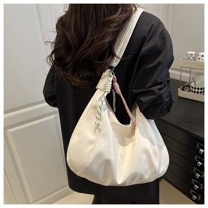 Dettaglio di una borsa hobo bianca lucida con un nodo intrecciato decorativo indossata