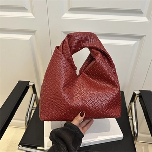 Minimalist red woven hobo bag with a knotted handle shown in a stylish modern room