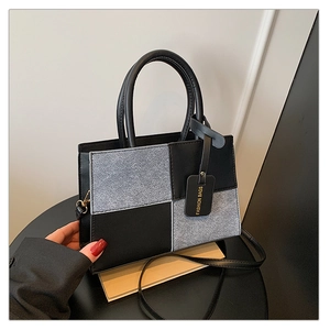 Detail of color-block tote bag with black leather, grey fabric, and gold buckles