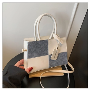 Detail view of contrast stitching and circular handles on a minimalist retro shoulder bag
