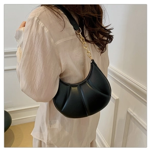 Detail of black pleated hobo bag with gold chain strap on shoulder in street style