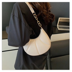 Detail of white pleated half-moon bag with gold chain strap worn by a model