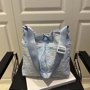 Borsa tote trapuntata azzurra con ricamo a onde e tracolla larga su libri bianchi