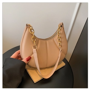 Detail of beige pleated crescent bag with gold chain and thin leather strap on a table