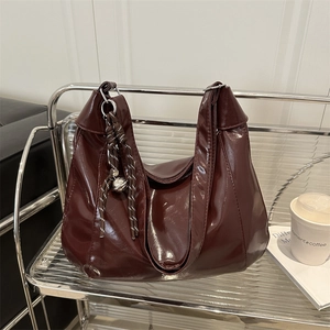 Chic burgundy patent leather hobo bag with wide shoulder strap on a silver stand