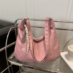 Pink glossy faux leather tote bag with tennis racket charm on a modern shelf