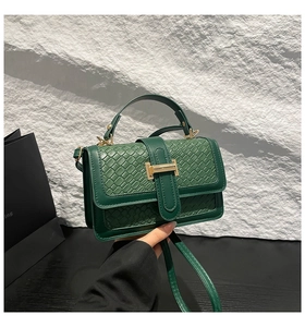 Detail of dark green woven crossbody bag featuring a golden H-clasp and leather texture
