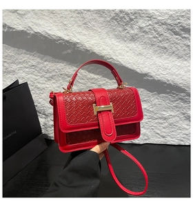 Detail of red woven leather handbag with a prominent golden H-shaped buckle closure