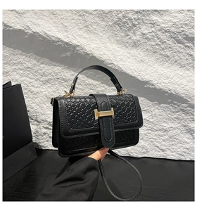 Close-up of woven texture black handbag featuring a signature gold H-buckle and top handle