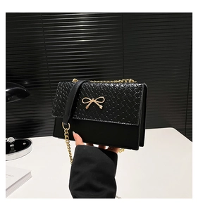 Detail of elegant black shoulder bag featuring gold bow buckle and woven leather texture