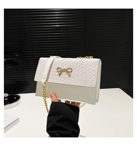 Close-up of white crossbody bag featuring woven texture flap and golden bow clasp