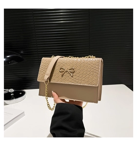 Detail of beige crossbody bag with woven texture, metal bow and gold chain strap