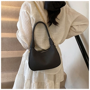 Detail of a black hobo shoulder bag with gold chain strap on a white pleated dress