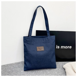Détail du sac cabas en denim bleu foncé avec étiquette en cuir marron et couture textile