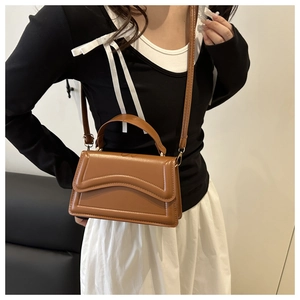 Close-up of brown rectangular handbag with wavy embossed patterns worn by model
