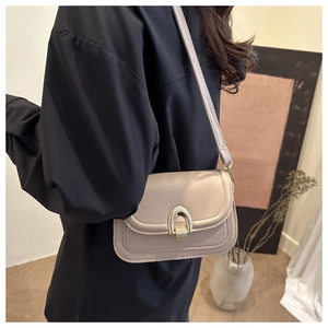 Detail of a beige saddle bag with a golden U-shaped buckle and fine stitching