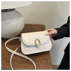 Close-up of cream faux leather saddle bag with golden U-shaped metal buckle and strap