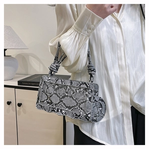 Detail of snake skin pattern handbag with wavy edge and knotted handle on a minimal background