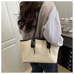 Detail of cream woven tote bag with black leather straps and knot accents on model
