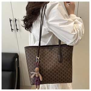 Detalle de un bolso tote de jacquard marrón con motivos M y colgante de conejo
