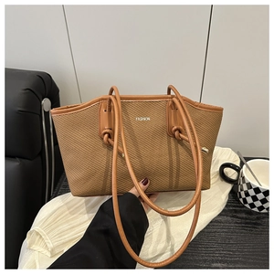 Detail of a brown woven tote bag featuring a white Fashion logo and leather long handles