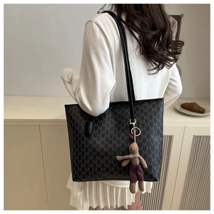 Detail of large black tote bag with M-pattern print and purple rabbit charm accessory