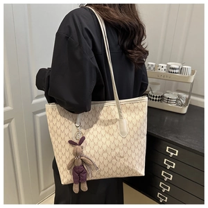 Close-up of beige tote bag with M-pattern print and cute plush rabbit charm detail