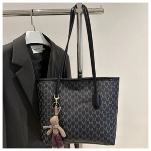 Detalle de bolso tote negro con estampado de monograma M y amuleto de conejo de peluche