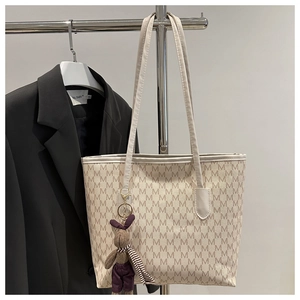 Detalle de bolso tote beige con estampado de letras M y colgante de peluche de conejo marrón