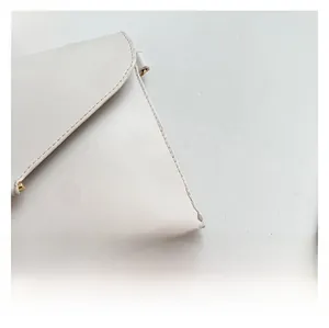 Gros plan d'un sac enveloppe en cuir blanc avec surpiqûres et chaîne dorée