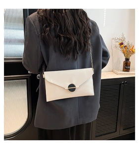 Détail du sac enveloppe blanc avec chaîne et boucle dorée sur un mannequin en blazer gris