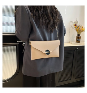 Sac bandoulière enveloppe beige chic avec chaîne dorée porté sur une femme en costume