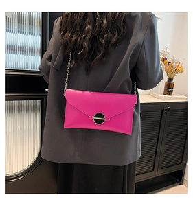 Détail d'un sac enveloppe magenta avec chaîne porté sur un blazer gris foncé
