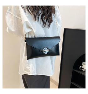 Vue latérale d'un sac enveloppe en cuir noir avec anneau métallique et chaîne dorée