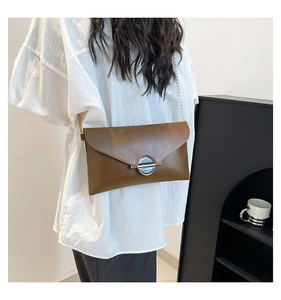 Détail du sac enveloppe en cuir marron foncé avec boucle ronde et bandoulière chaîne