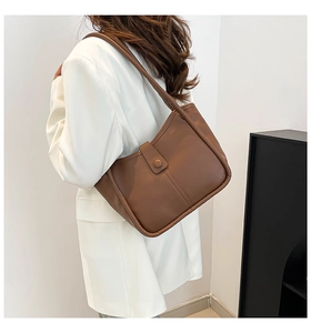 Detail of dark brown tote bag with vertical stitching and buckle on a white blazer