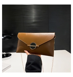 Détail de la pochette enveloppe en cuir marron avec boucle dorée et bandoulière chaîne