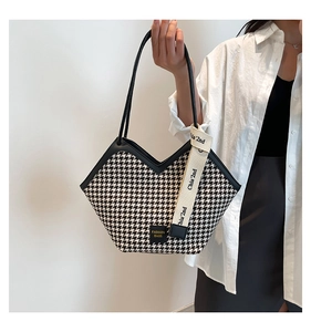 Detail of houndstooth tote bag with leather straps and decorative fashion ribbon
