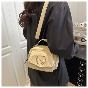Close-up of beige corduroy crossbody bag with cute bear embroidery and woven shoulder strap