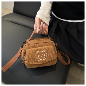 Detail of brown corduroy crossbody bag featuring a white embroidered bear pattern