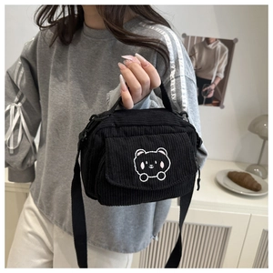 Close-up of black corduroy messenger bag with a minimalist white bear embroidery detail